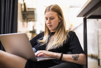 En ung kvinna sitter i en fåtölj och tittar på sin laptop.