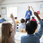 Två flickor håller upp handen i klassrum