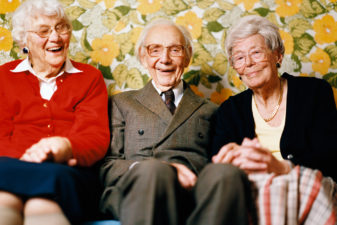 En äldre man och två äldre kvinnor skrattar tillsammans i soffa