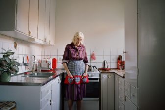 Äldre kvinna med förkläde står i kök