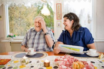 Foto på en äldre man och kvinna från hemtjänsten som skrattar tillsammans.