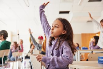 Flicka i klassrum räcker upp handen