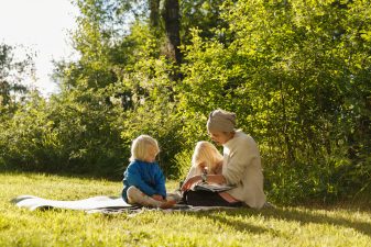 Children and adult reading in a grass field