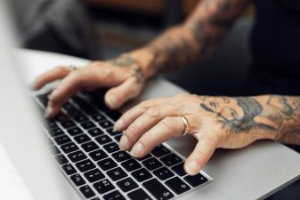 Person with tattoos writing on laptop