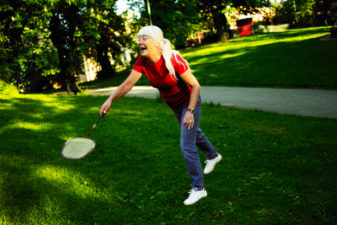 Older woman playing badminton on a lawn.