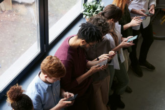 Flera personer står bredvid varandra och tittar i mobilen