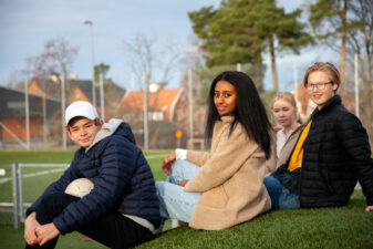 Ett gäng ungdomar sitter på en gräskulle på skolgården.